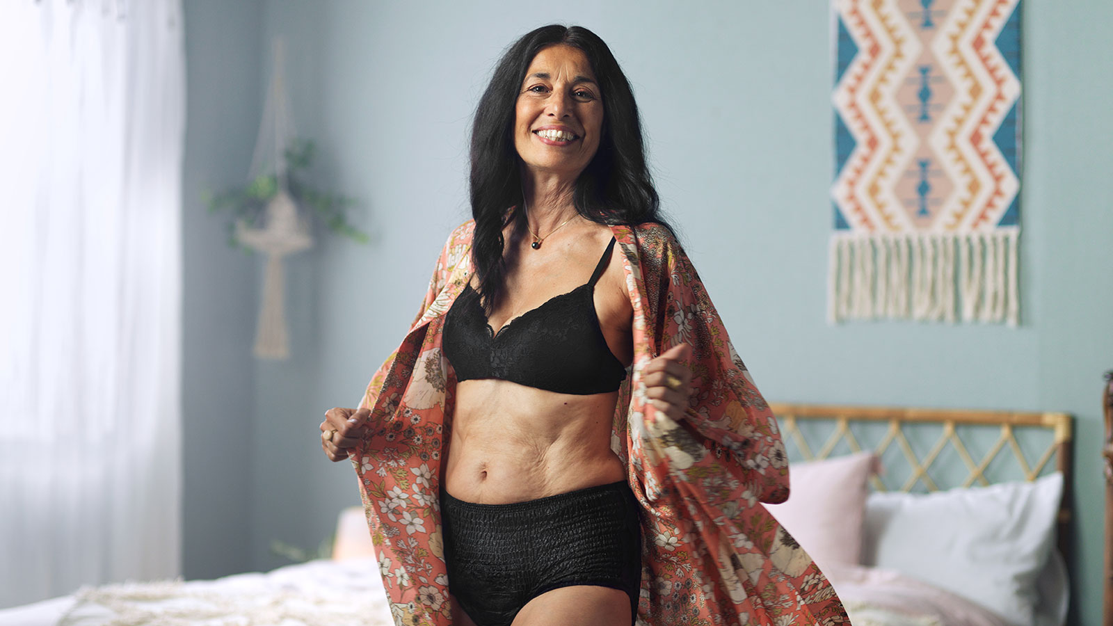 Selvsikker kvinde står foran en seng og smiler Selvsikker kvinde står foran en seng og smiler